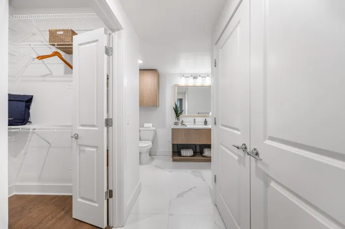 Modern apartment bathroom with elegant vanity, stylish cabinet, and spacious walk-in closet featuring wooden flooring.
