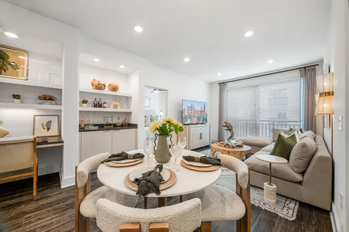 Contemporary living room with plush sofa, chic dining setup, and sleek shelving, accentuated by natural light from large windows.