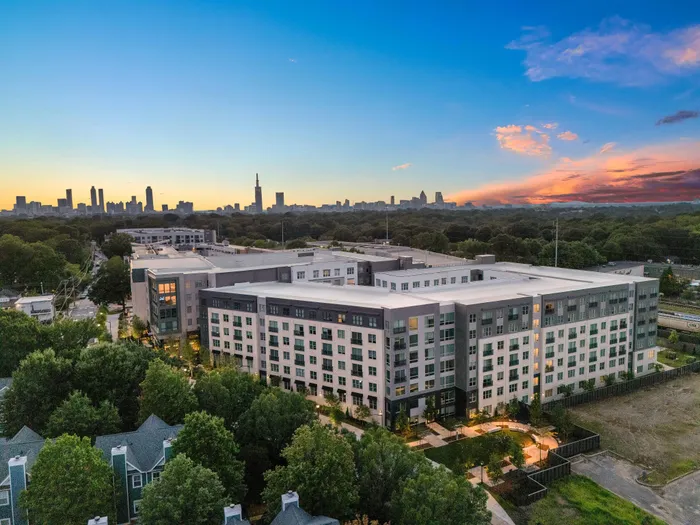 Chic urban apartment complex with modern design, surrounded by lush greenery and offering stunning sunset views of the city skyline.