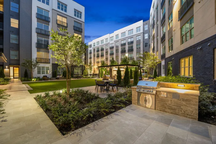 Charming urban courtyard with modern apartment views, featuring lush landscaping, a sleek outdoor grill, and cozy seating under a pergola.