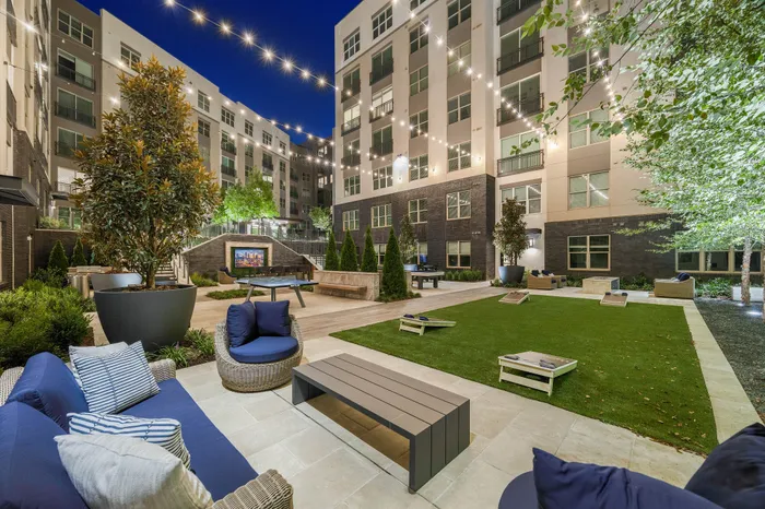 Chic apartment courtyard at night featuring cozy seating, lush greenery, and elegant string lights for a welcoming ambiance.