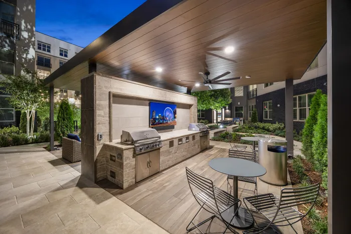 Luxurious outdoor kitchen with high-end grills, cozy seating, and modern lighting in a beautifully landscaped apartment courtyard.