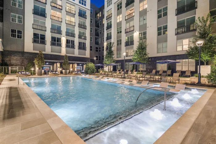 Luxurious apartment complex with a beautifully illuminated pool, surrounded by modern architecture and lush greenery, perfect for a relaxing evening swim.