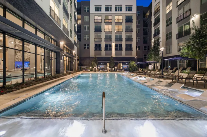 Luxury apartment complex with a stunning outdoor swimming pool, surrounded by elegant lounge chairs and ambient evening lighting.