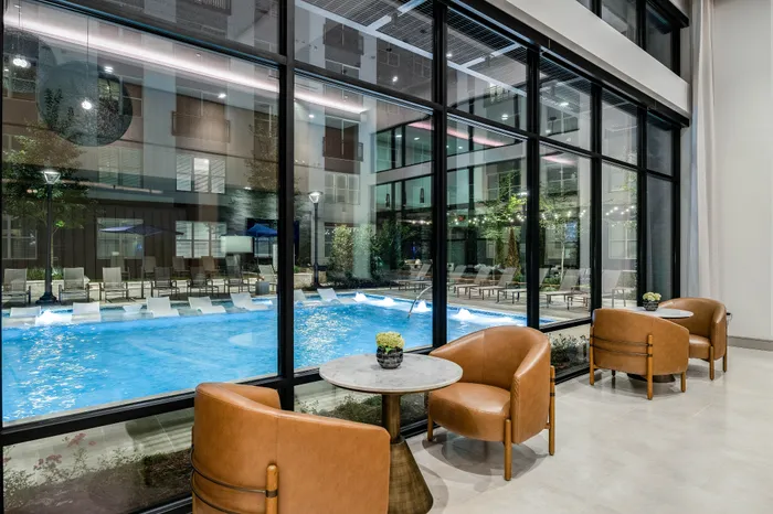 Elegant lounge area with plush leather chairs and a view of a sparkling outdoor pool, surrounded by modern architectural details.