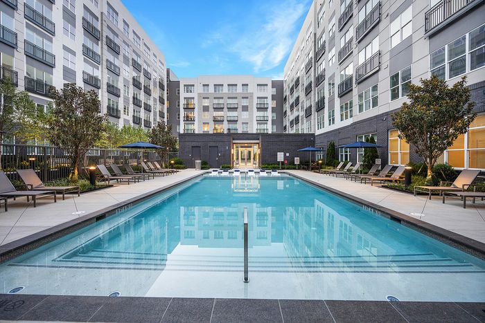 Luxurious apartment complex featuring a sparkling pool surrounded by elegant lounge chairs and lush landscaping, set against a modern architectural backdrop.