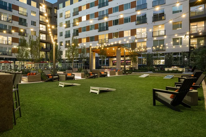 Charming apartment courtyard at night with cozy outdoor seating, ambient string lights, and lush greenery.