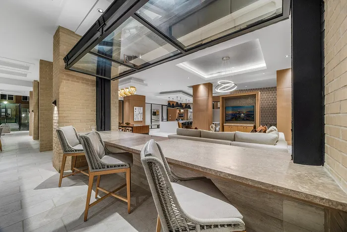 Modern open living space with elegant brick walls, plush seating area, and sleek kitchen featuring pendant lighting. Spacious design ideal for comfort and style.