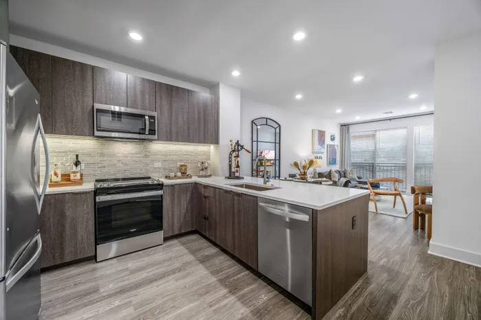 Sleek modern kitchen with wooden cabinetry, stainless steel appliances, and an open-layout living room filled with natural light, perfect for entertaining.