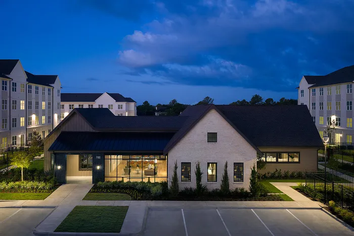 Charming apartment complex at dusk featuring modern architecture, well-lit surroundings, and manicured landscaping under a picturesque evening sky.