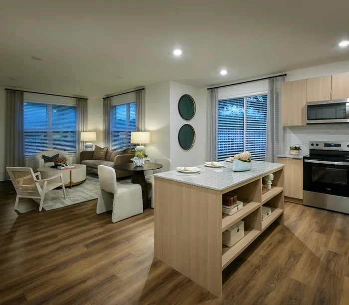 Modern open-plan living area featuring a cozy seating space, elegant dining set, and sleek kitchen with island. Large windows and stylish wood flooring enhance the inviting ambiance.