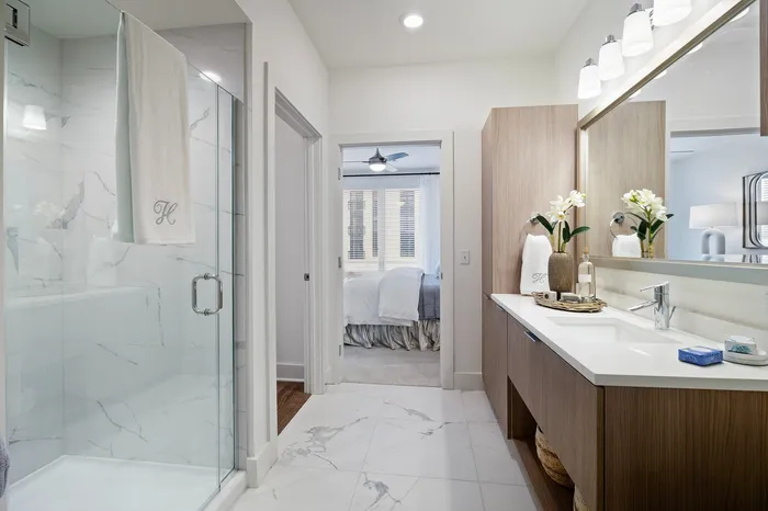 Elegant bathroom with sleek marble flooring, a glass shower, and stylish vanity flowing into a cozy, well-lit bedroom.