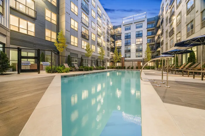 Luxurious apartment complex featuring a sparkling outdoor pool, surrounded by modern architecture and ambient lighting.