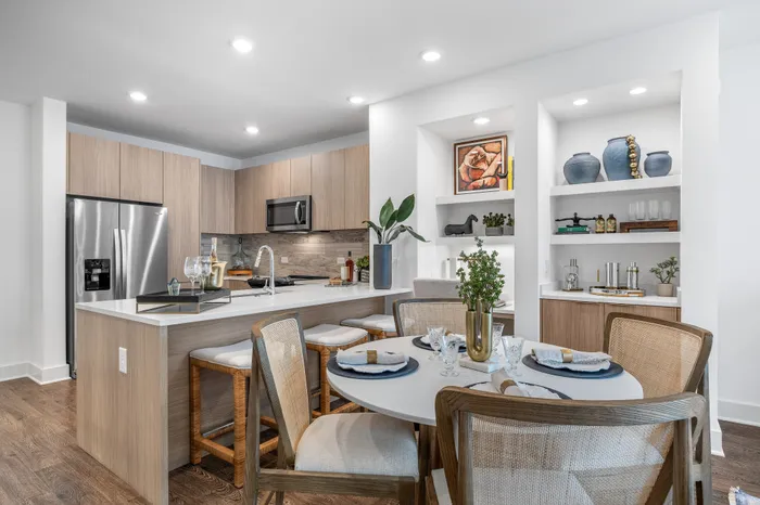 Modern kitchen and dining area featuring sleek wood cabinetry, elegant island with bar seating, and a beautifully set round table surrounded by stylish chairs.