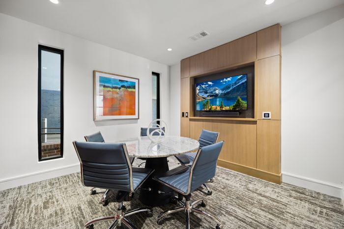 Elegant conference room with a sleek marble table, modern blue chairs, vibrant artwork, and a scenic wall-mounted TV.