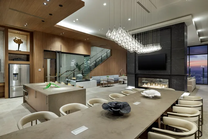 Luxurious open-plan living space with sleek modern kitchen, elegant dining area, and cozy fireplace under stunning chandelier lighting.