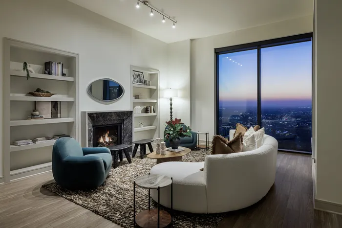 Elegant living room with cozy fireplace, chic furniture, and breathtaking city view from large windows.