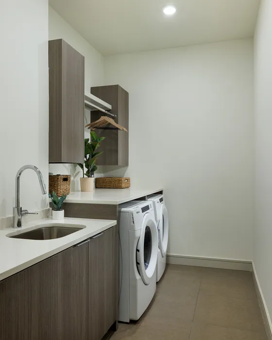 Modern laundry room featuring sleek cabinets, built-in washer and dryer, and elegant countertop with sink.
