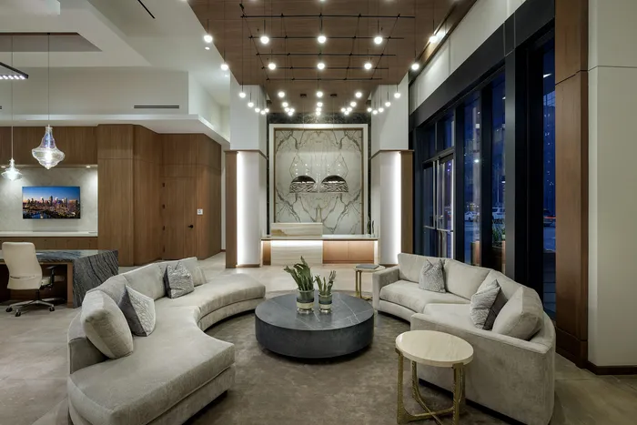 Elegant lobby space featuring plush curved sofas, a modern round coffee table, and striking ceiling lights with a sophisticated marble accent wall.