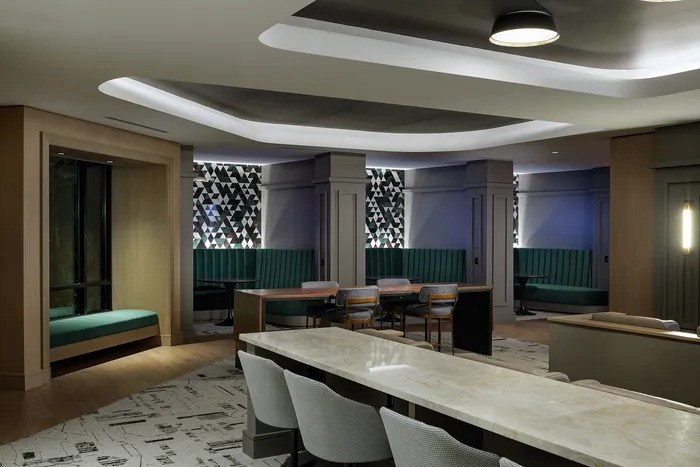Elegant lounge area with modern decor, featuring plush turquoise seating, geometric wall designs, and a sleek marble countertop.