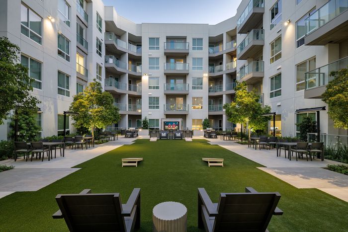 Contemporary apartment courtyard with lush greenery, outdoor seating, and modern building facade.