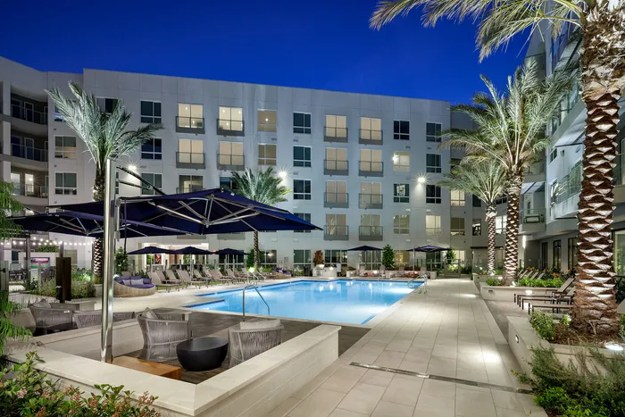 Luxurious apartment complex showcasing a sparkling pool, elegant seating areas, and tall palm trees at night.