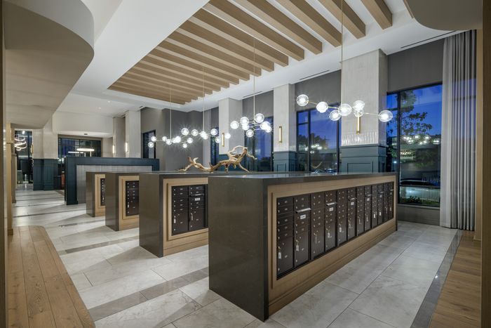 Elegant apartment lobby with modern chandeliers, stylish mailboxes, and large windows showcasing a stunning evening view.