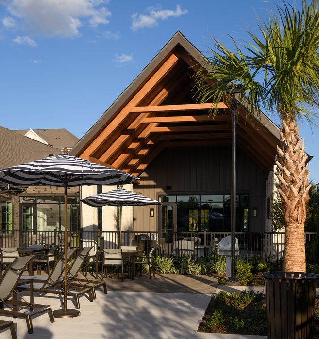 Inviting outdoor patio with stylish striped umbrellas and contemporary seating against a backdrop of lush greenery and a modern building with wooden accents.