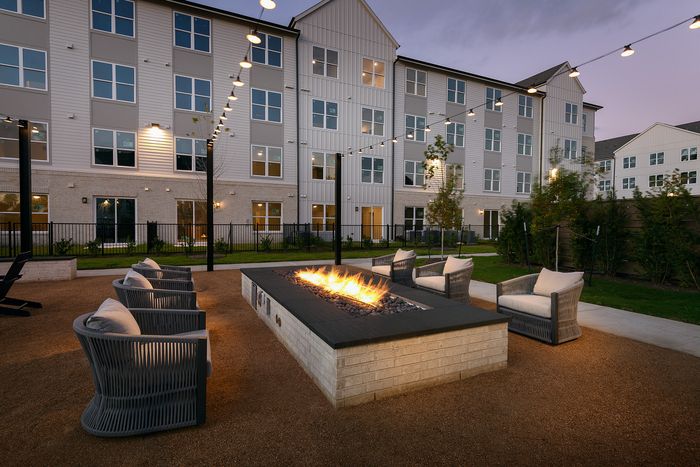 Elegant outdoor fire pit area with cozy seating and modern apartment building backdrop, perfect for relaxing evenings.