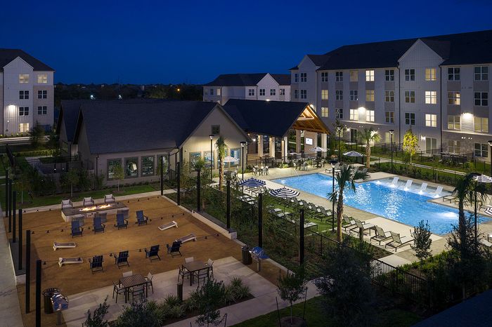 Luxurious apartment complex at night featuring a beautifully illuminated pool, cozy fire pit, and elegant outdoor seating area.