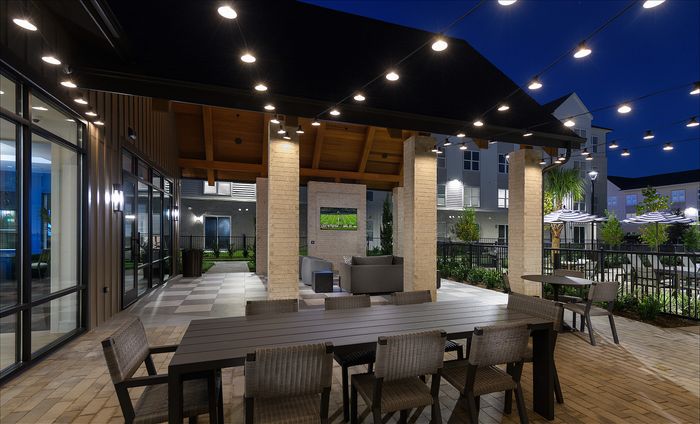 Chic outdoor patio at night with elegant seating, ambient string lights, and a cozy TV area, perfect for entertaining.