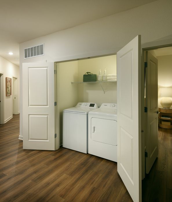 Chic apartment hallway featuring in-unit laundry with sleek washer and dryer, complemented by elegant wood flooring.
