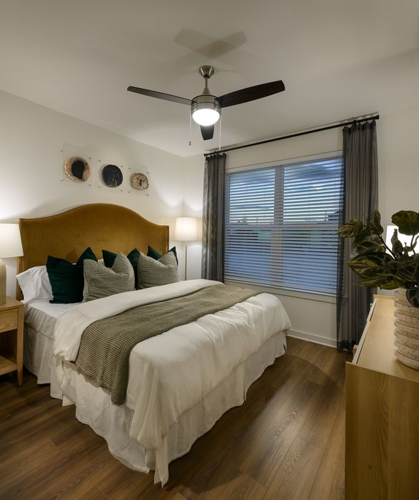 Inviting bedroom with elegant hardwood floors, a plush bed with modern decor, and ample natural light from a large window.