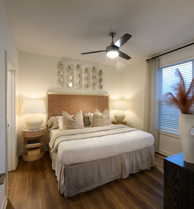 Elegant bedroom with cozy bedding, wooden floors, modern ceiling fan, and chic decor creating a serene ambiance.