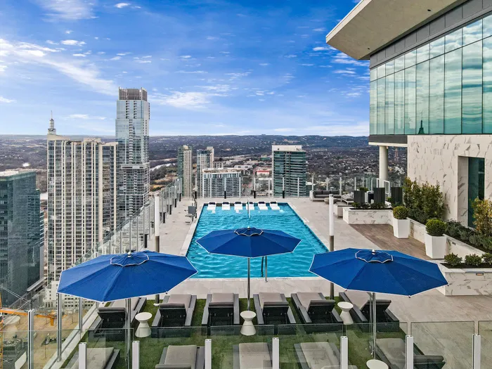 Luxurious rooftop pool with stunning city skyline views, featuring plush lounge chairs and vibrant blue umbrellas.