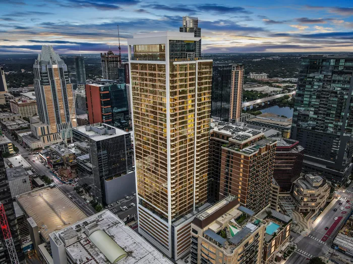 Stunning aerial view of a modern high-rise apartment building in a bustling cityscape at sunset, showcasing vibrant city life with nearby architectural landmarks.