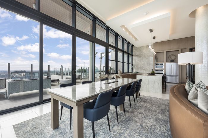 Luxurious open-concept kitchen and dining area featuring floor-to-ceiling windows with stunning views, elegant marble island, and plush seating for a sophisticated urban experience.