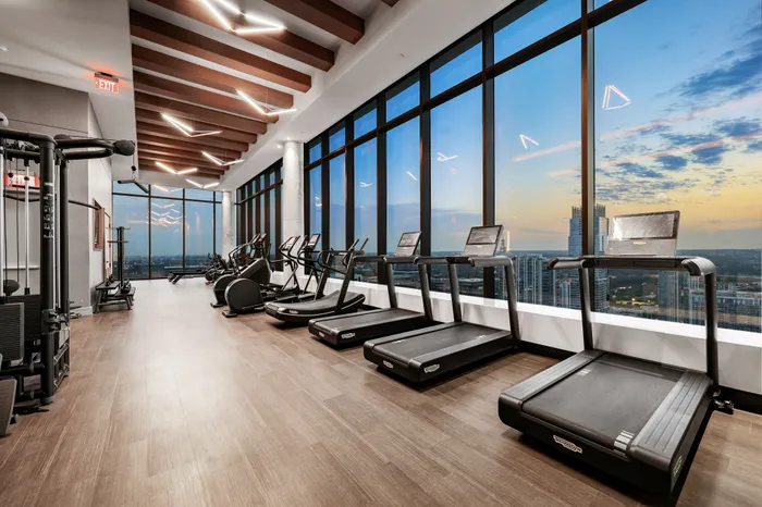 Luxury gym with stunning city views, featuring state-of-the-art treadmills and modern fitness equipment, illuminated by elegant ceiling lights.