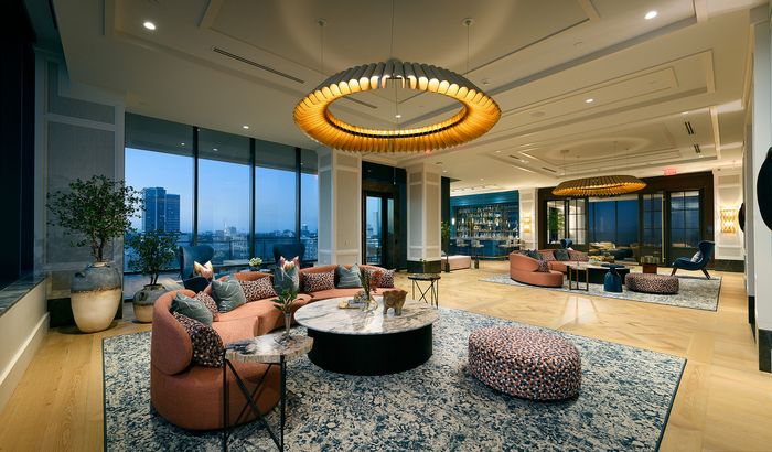 Luxurious and inviting lounge area with modern furnishings, elegant circular chandelier, and expansive city views through floor-to-ceiling windows.