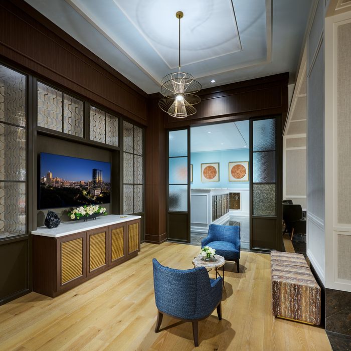 Elegant lounge area with modern lighting, featuring blue chairs, a wooden floor, and a large TV displaying a cityscape.