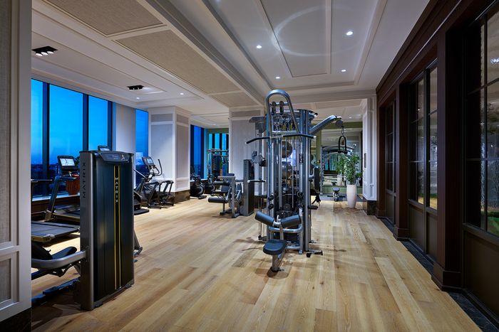 Elegant fitness center with state-of-the-art equipment, large windows offering panoramic views, and a sleek wooden floor for a luxurious workout experience.