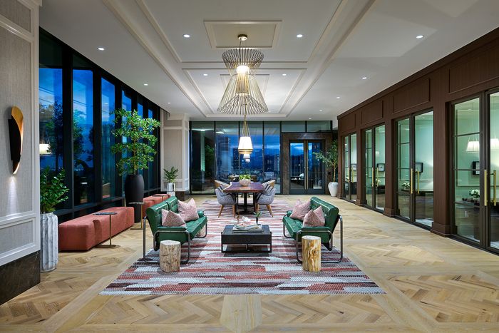 Luxurious and spacious living area with elegant wood flooring, stylish green sofas, and large floor-to-ceiling windows offering a breathtaking city view.