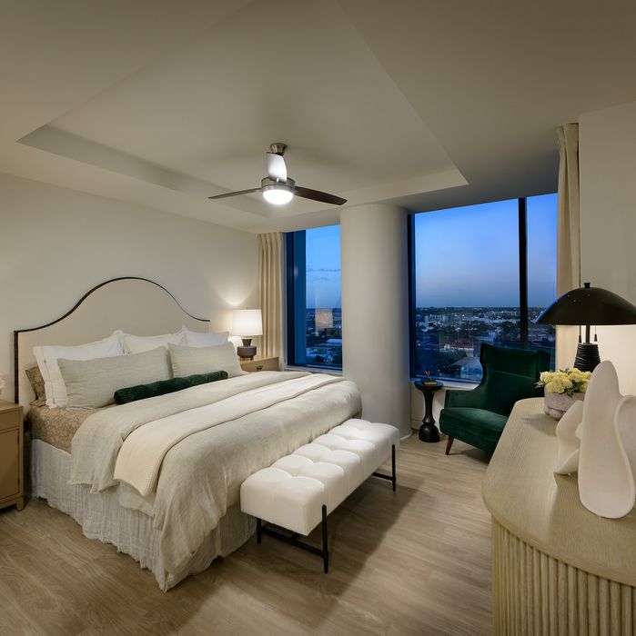 Luxurious bedroom with a king-sized bed, elegant decor, and a stunning city view from a large window.