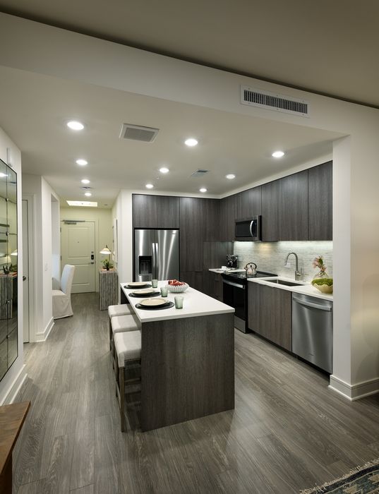 Modern kitchen design featuring sleek dark wood cabinets, stainless steel appliances, and a spacious island with seating under elegant recessed lighting.