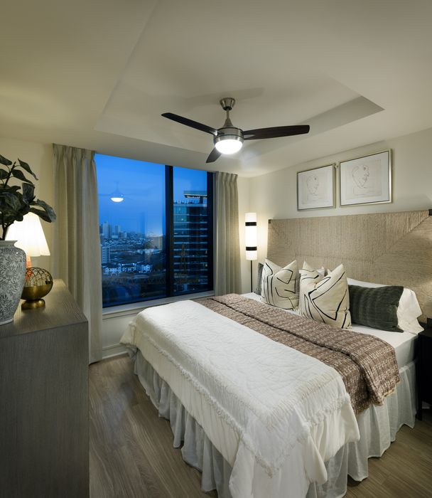 Elegant bedroom with a stylish ceiling fan, large window offering city views, and chic decor elements for a luxurious urban living experience.