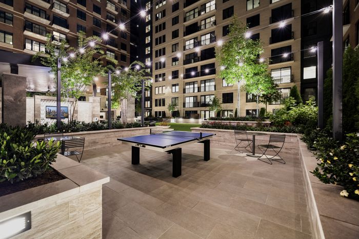 Elegant urban courtyard with modern amenities including table tennis under ambient string lights, surrounded by lush greenery and contemporary architecture.