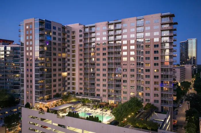 Modern high-rise apartment complex at dusk featuring stunning city views, illuminated windows, and an inviting outdoor pool area.