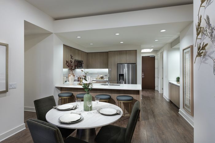 Modern kitchen and dining area featuring sleek countertops, stylish bar stools, and an elegant round dining table set with fine dinnerware.