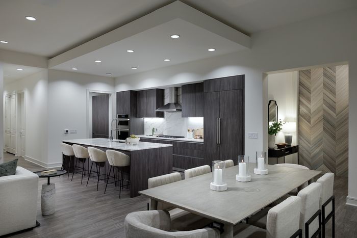Contemporary apartment kitchen and dining area featuring sleek dark cabinetry, a large center island with plush stools, and a stylish dining table set for elegant gatherings.