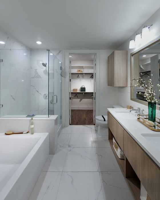 Elegant modern bathroom featuring a luxurious glass shower, marble tiles, and spacious vanity leading to a walk-in closet.